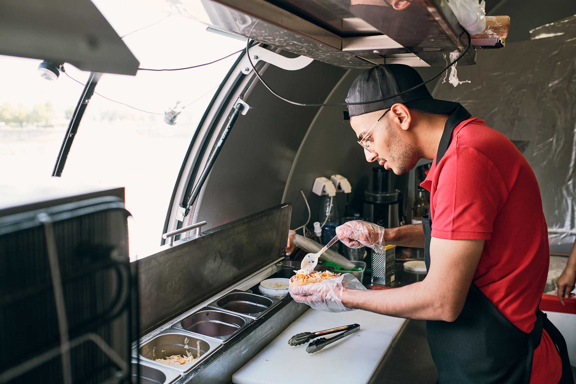 young-man-in-uniform-cooking-tasty-hotdogs-in-food